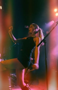 a woman in black dress singing on stage with microphone and lights behind her at a concert