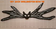 a black and white cat brooch sitting on top of a piece of paper with the words diy jack skeleton bow tie