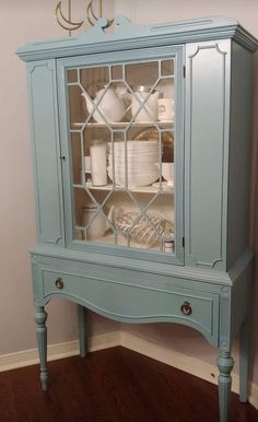 a blue china cabinet with glass doors on the top and bottom shelves, in front of a wall