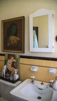 a bathroom with a sink, mirror and painting on the wall above it's toilet