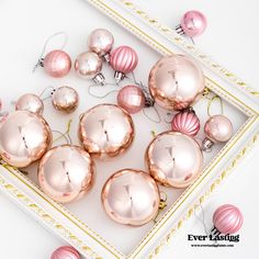 pink and gold ornaments are arranged on a white tray with golden trimmings around them