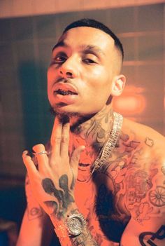 a man with lots of tattoos on his chest and hands in front of his face