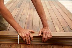 a man is holding onto a wooden decking board with one hand and the other hand on top of it