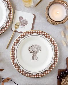 the table is set for thanksgiving dinner with turkey plates and place settings on it, along with candles