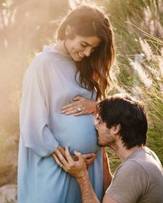 a pregnant man kissing the belly of a pregnant woman