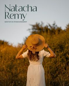 a woman in a white dress and straw hat stands in tall grass with her hands on her head