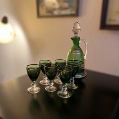 a green glass pitcher and four glasses on a table with a lamp in the background