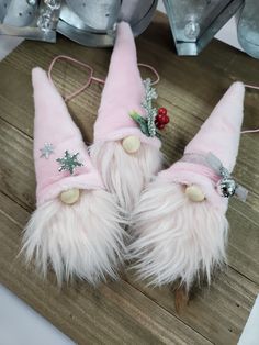 three pink and white christmas gnome hats on top of a wooden table next to silver bells