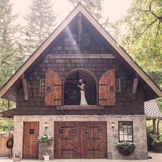 a bride and groom are standing in the window of a rustic cabin style house with wood shutters