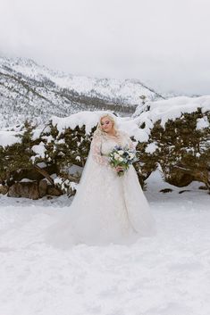 a woman in a wedding dress standing in the snow with her bouquet on her hand