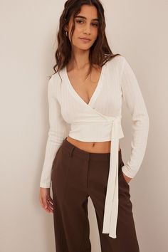 This top is ribbed and features a wrapped V-neck. It has long sleeves and a tie strap on the waist. This top features a stretchy slim fit. Wrap Top Outfit, Movie Core, Long Sleeve Top Outfit, Long Sleeve Wrap Top, Flattering Outfits, High Neck Designs, White Long Sleeve Top, Fitted Turtleneck, Chunky Knits Sweater