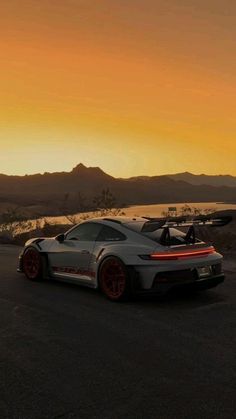 a grey sports car parked on the side of a road at sunset with mountains in the background