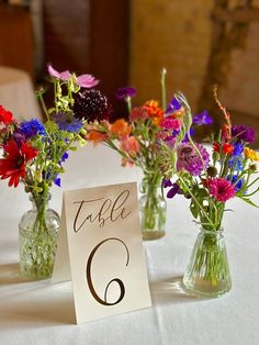 three vases filled with colorful flowers sitting on top of a white tablecloth covered table