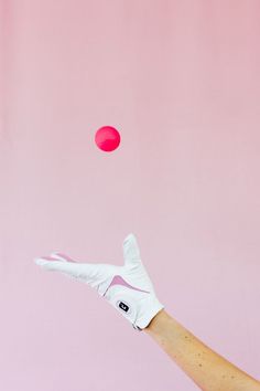 a person's hand wearing white gloves throwing a pink ball into the air with their fingers