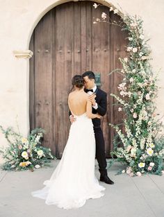 a bride and groom standing in front of a wooden door with flowers on the side