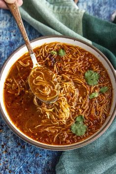 a person holding a spoon full of noodles and chili sauce with cilantro on the side