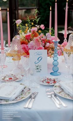 the table is set with pink flowers, candles and place settings for two people to sit at