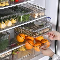 a person reaching into an open refrigerator with fruits and vegetables in the door, including oranges