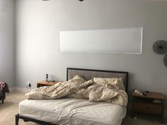 an unmade bed in a room with a fan on the wall and a window