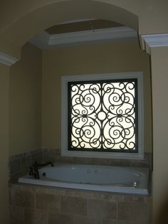 a bath tub sitting under a window next to a tiled bathroom floor and walls with decorative ironwork on the windowsill