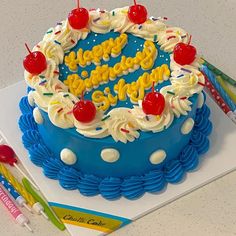 a blue birthday cake with white frosting and cherries on top, surrounded by colorful markers