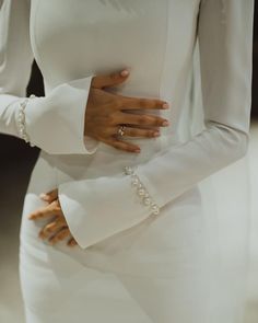 a woman in a white dress is holding her stomach with both hands and wearing pearls