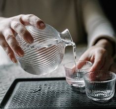 someone pouring water into two glasses on a tray