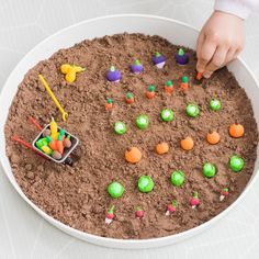 a child's hand picking up candy from a bowl filled with dirt and candies