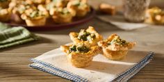 three mini quiche cups sitting on top of a napkin next to a bowl of broccoli