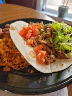 two tacos with meat, tomatoes and lettuce are on a black plate