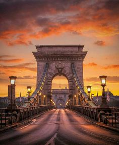 the sun is setting over the bridge and street lamps are lit up on both sides