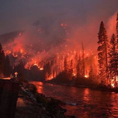 the fire is burning in the mountains and trees near a river that has water running through it