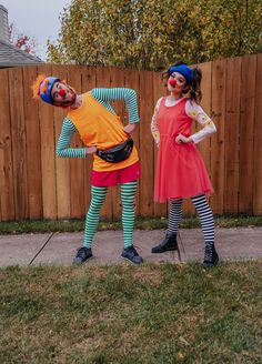 two people dressed up as clowns standing in front of a fence with their arms around each other