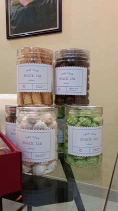 jars filled with different types of cookies on top of a glass table next to a painting