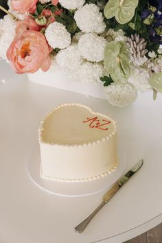 a heart shaped cake sitting on top of a table next to flowers and a knife