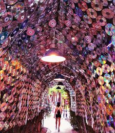 a woman walking through a tunnel covered in cds