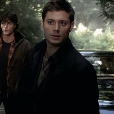 two young men standing next to each other in front of a parked car and trees