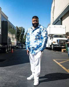 a man standing in the middle of a parking lot wearing white pants and a blue shirt