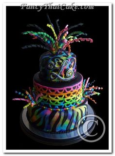 a multi - colored cake decorated with feathers and beads on a black tablecloth covered plate