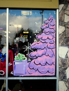 a window with a christmas tree painted on the side and presents in front of it