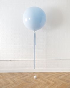 a blue balloon floating in the air on a wooden floor next to a white brick wall