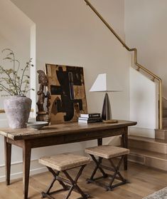 a wooden table with two stools next to it and a painting on the wall