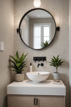 a white sink sitting under a round mirror next to a potted plant on top of a counter