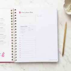 an open planner with pink flowers on it next to a cup of coffee and a pen