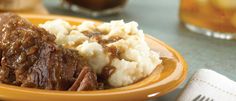 a yellow plate topped with meat and mashed potatoes next to a glass of beer