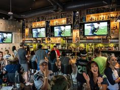 a group of people standing in front of televisions at a bar with sports memorabilia on the walls