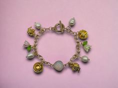 This baroque charm bracelet is made with gold toned teacups, teapots, pearls and lily of the valley flower charms.  - approx 8 inches long  - toggle closure  Materials are made from alloy metal and plastic. Whimsical Gold Charm Bracelet, Handmade Charm Bracelets, Lily Of The Valley Flowers, Valley Flowers, Handmade Charms, Flower Charm, Lily Of The Valley, Baroque Pearls, Charm Bracelets