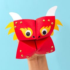 someone is holding up a red origami mask with horns and eyes on it