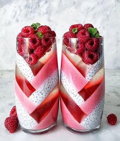 two glasses filled with raspberries on top of a table next to each other