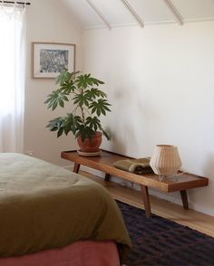 a bed room with a neatly made bed and a potted plant on a table